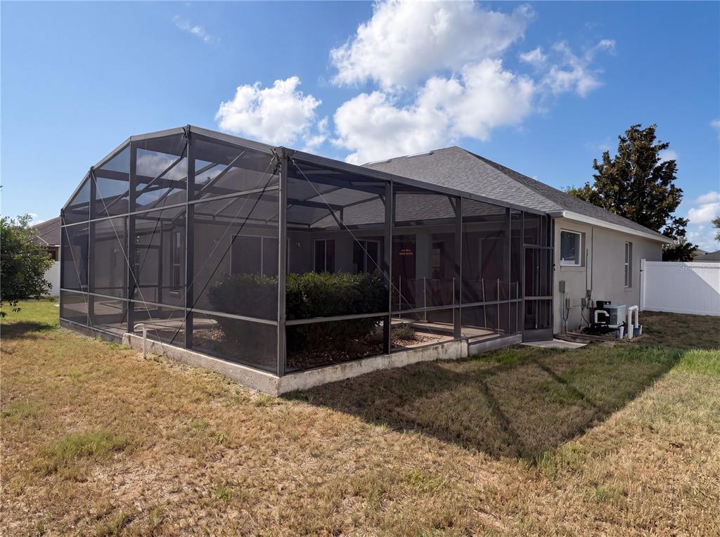 The exterior of a house features a large screened-in patio enclosure and a grassy backyard — 457 AMETHYST AVENUE, AUBURNDALE, FL