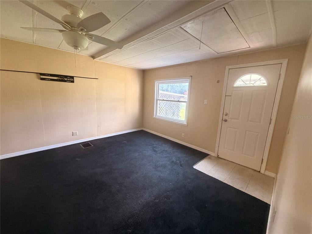 A room with tan walls, black carpeting, a ceiling fan, and a white entry door — 6345 SE 110TH STREET UNIT 1, BELLEVIEW, FL
