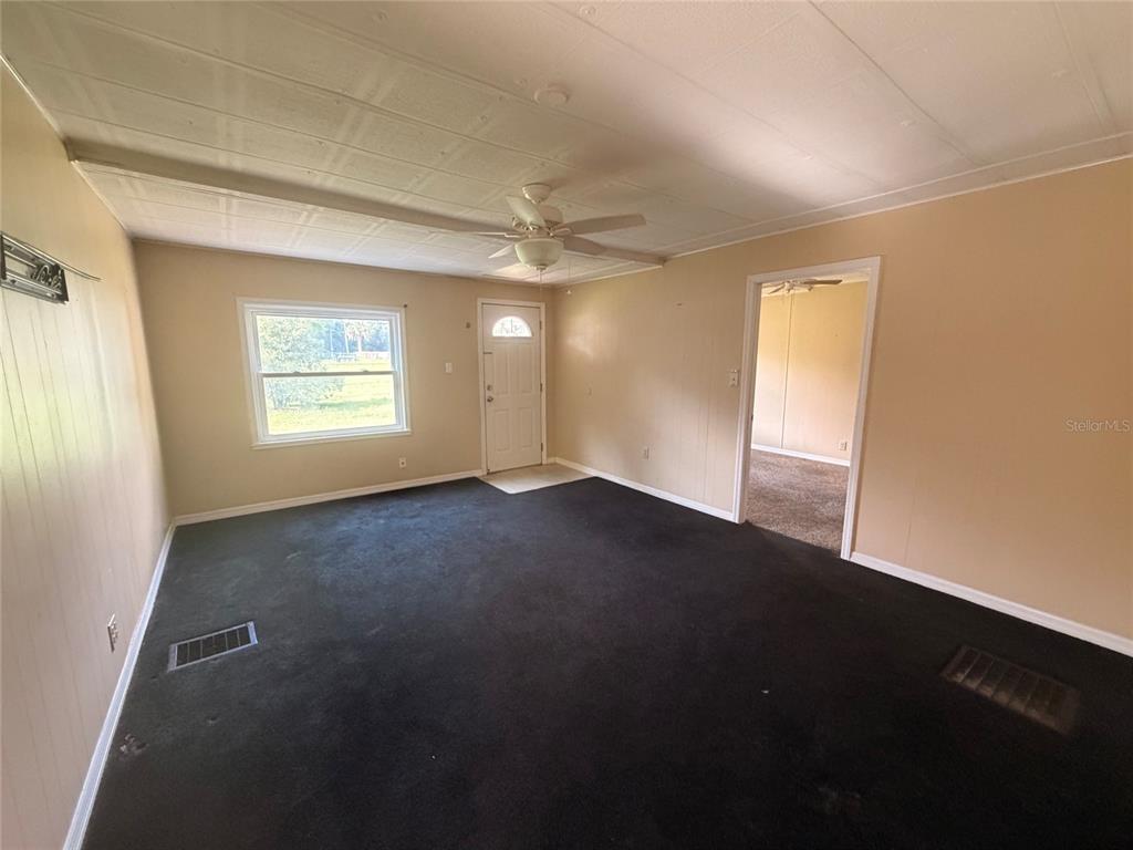 A living room with beige walls, dark carpeting, a ceiling fan, and an exterior door — 6345 SE 110TH STREET UNIT 1, BELLEVIEW, FL