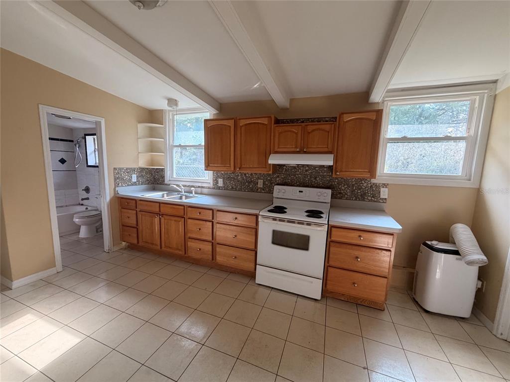 A kitchen features wood cabinets, white appliances, a tiled backsplash, and light-colored floor tiles — 6345 SE 110TH STREET UNIT 1, BELLEVIEW, FL