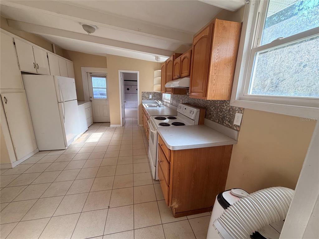 A kitchen features light tile flooring, wood cabinets, white appliances, and a tiled backsplash — 6345 SE 110TH STREET UNIT 1, BELLEVIEW, FL