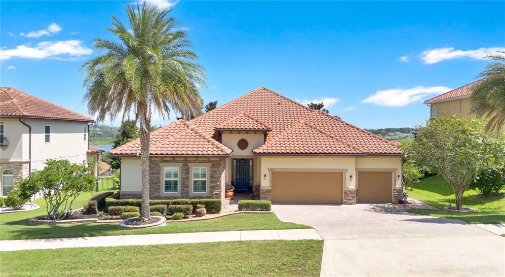 A single-story house with a tile roof, stone facade, and a three-car garage — 1744 BELLA LAGO DRIVE, CLERMONT, FL