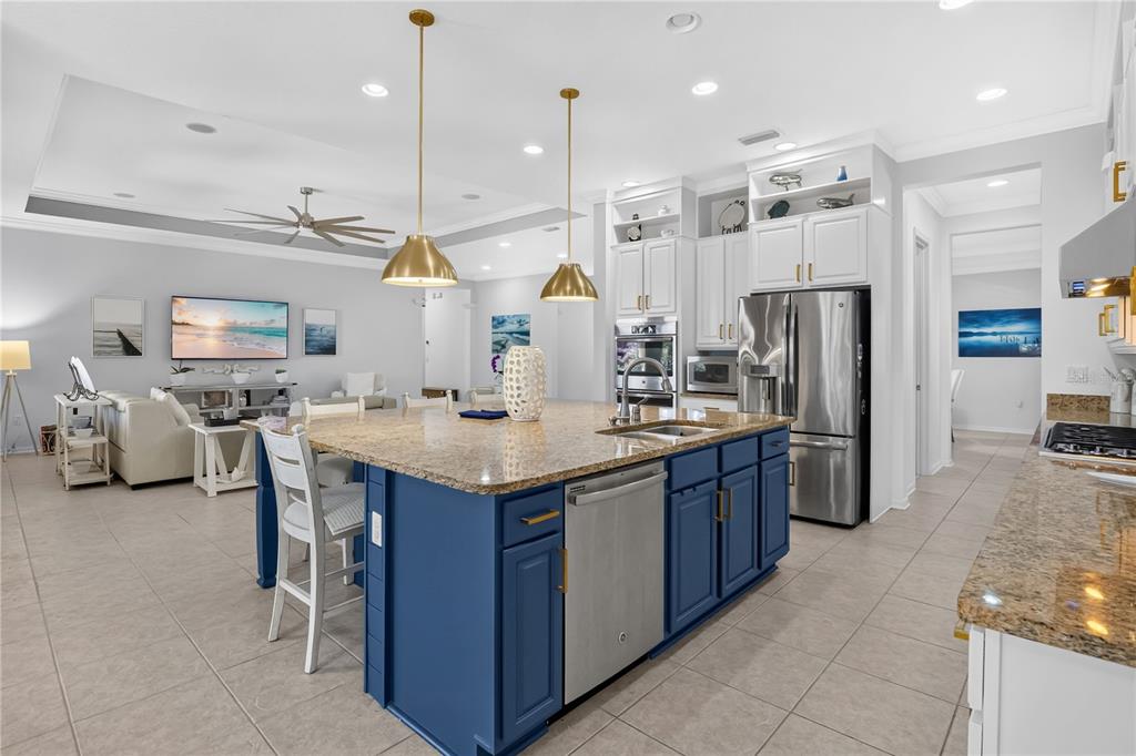A kitchen with a blue island, granite countertops, and stainless steel appliances opens to a living area — 1744 BELLA LAGO DRIVE, CLERMONT, FL