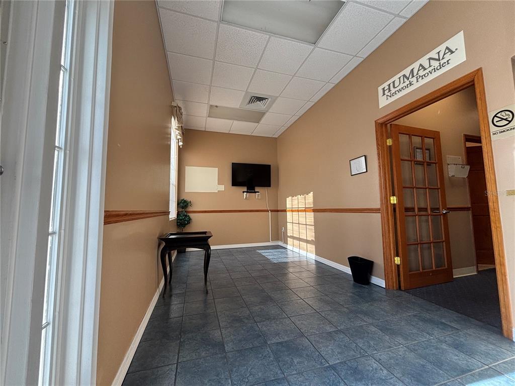 A waiting room features tan walls, dark tile flooring, a wall-mounted television, and a wooden door — 2855 ALT 19, PALM HARBOR, FL