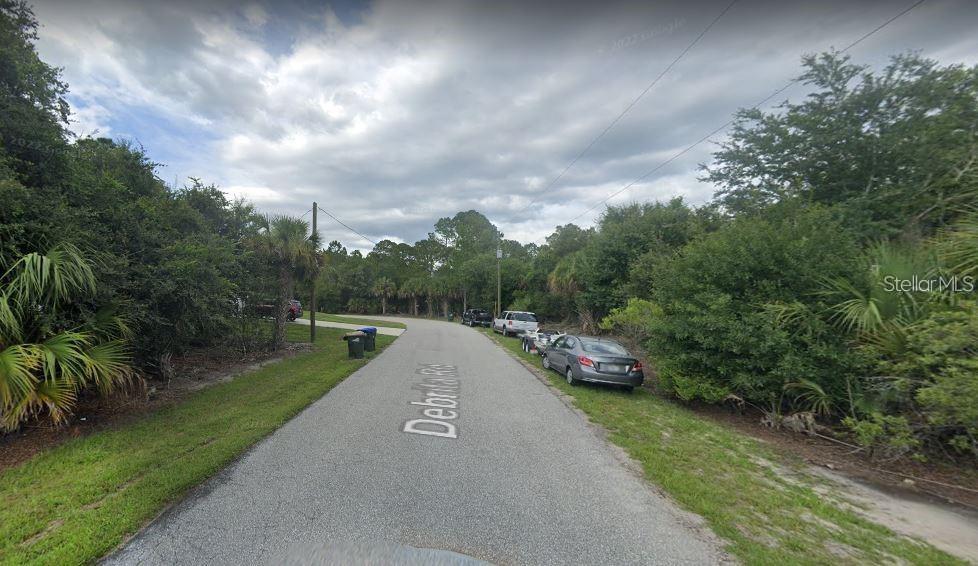 A paved road winds through a wooded residential area with parked cars and trash bins — 0 DE BRITA ROAD, NORTH PORT, FL