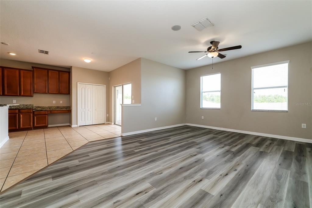 An open-concept living area features wood-look flooring, a ceiling fan, and an adjacent tiled kitchen — 2320 DOVESONG TRACE DRIVE, RUSKIN, FL