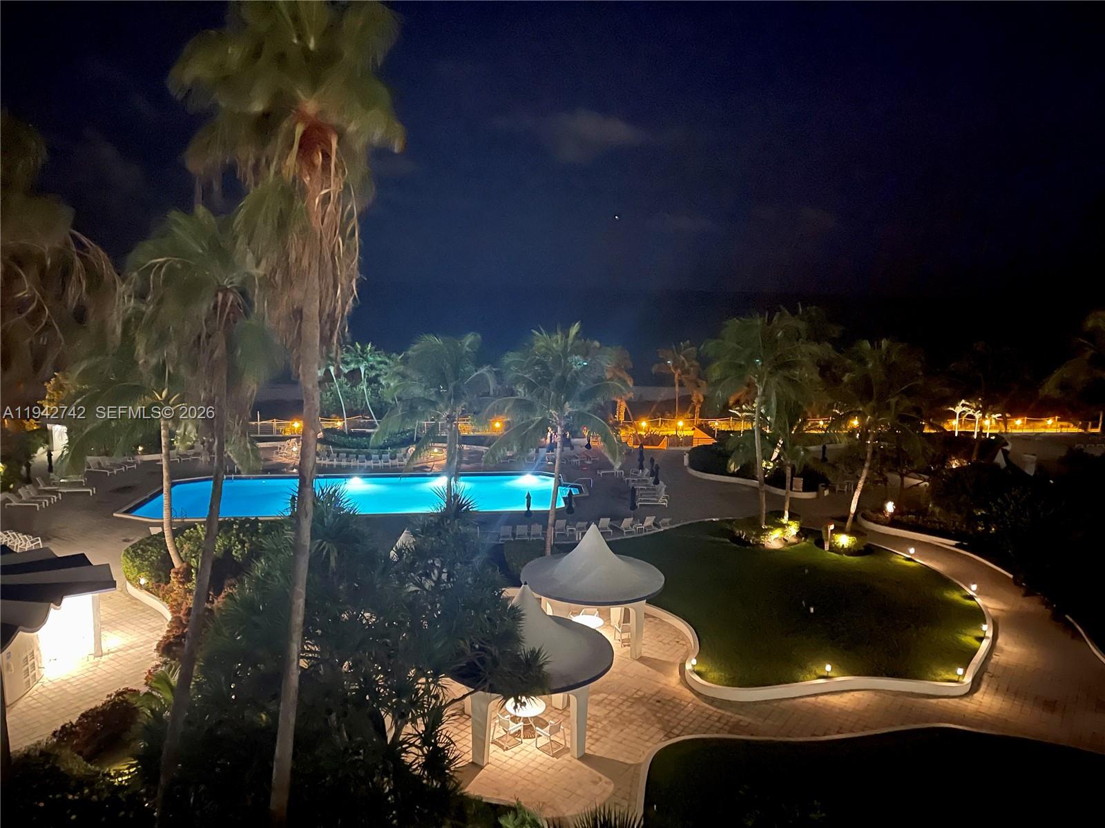 An elevated night view of a swimming pool, palm trees, and landscaped grounds — 5161 Collins Ave # 715, Miami Beach FL 33140, MIAMI BEACH, FL
