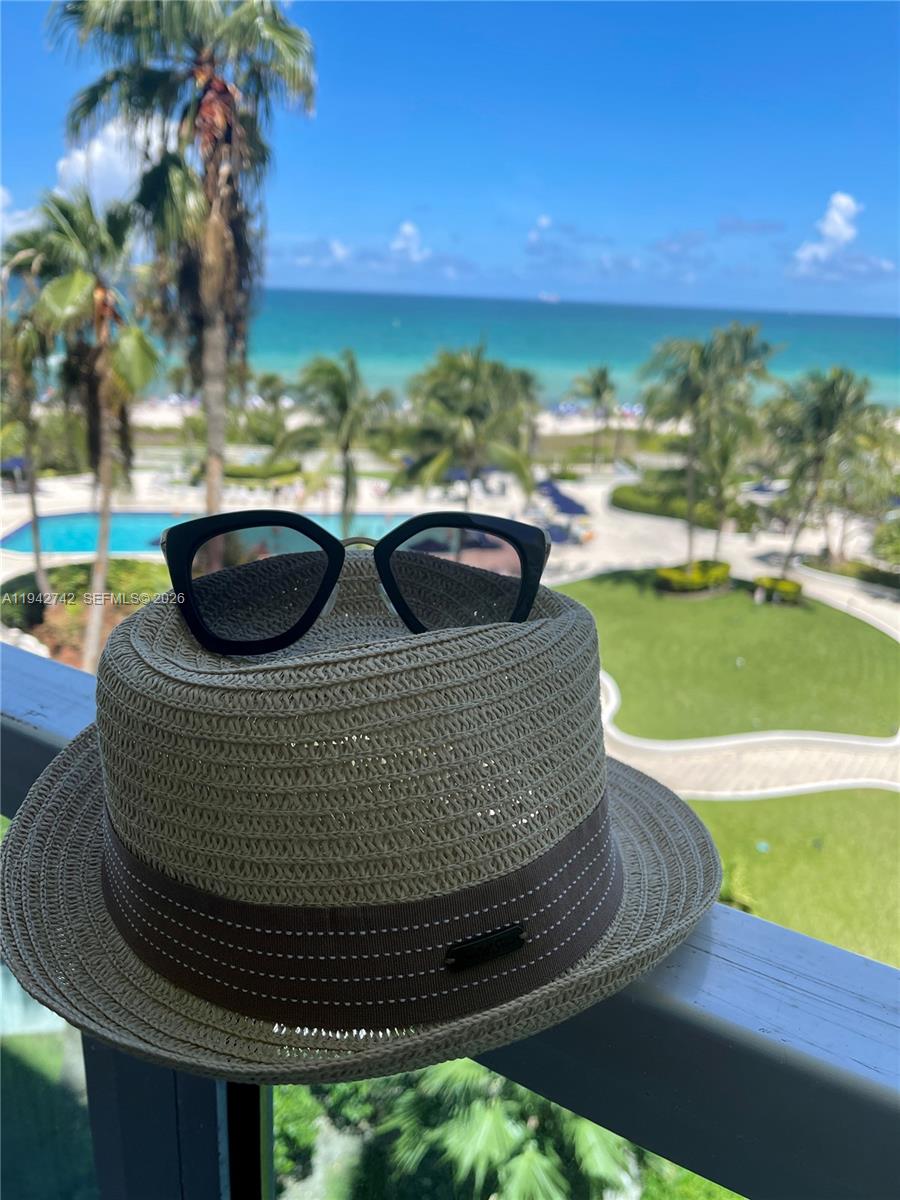 A straw fedora with sunglasses rests on a balcony railing overlooking a tropical beach — 5161 Collins Ave # 715, Miami Beach FL 33140, MIAMI BEACH, FL