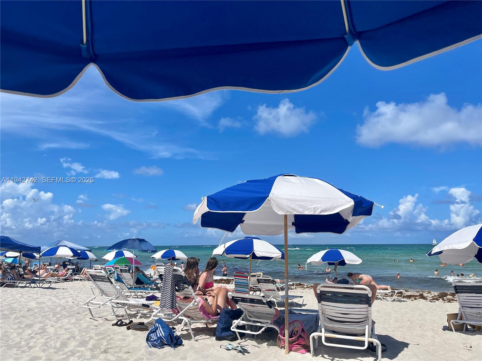 A beach scene features multiple umbrellas and lounge chairs under a bright blue sky — 5161 Collins Ave # 715, Miami Beach FL 33140, MIAMI BEACH, FL