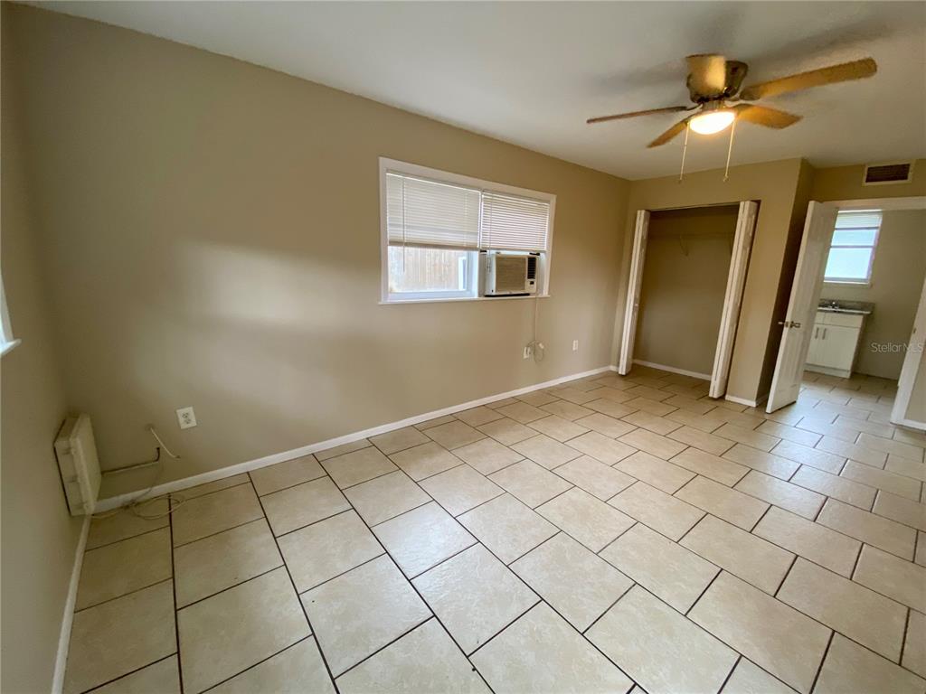 A bedroom features beige walls, light-colored tile flooring, a ceiling fan, and a window unit — 38313 TUCKER ROAD, ZEPHYRHILLS, FL
