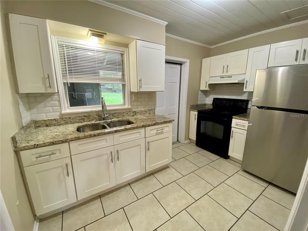 A kitchen features white cabinets, granite countertops, a stainless steel refrigerator, and tiled flooring — 38313 TUCKER ROAD, ZEPHYRHILLS, FL