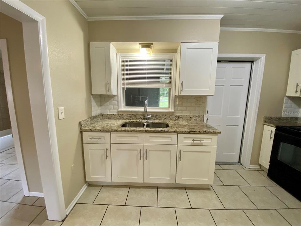 A kitchen features white cabinets, granite countertops, a double sink, and a tiled backsplash — 38313 TUCKER ROAD, ZEPHYRHILLS, FL