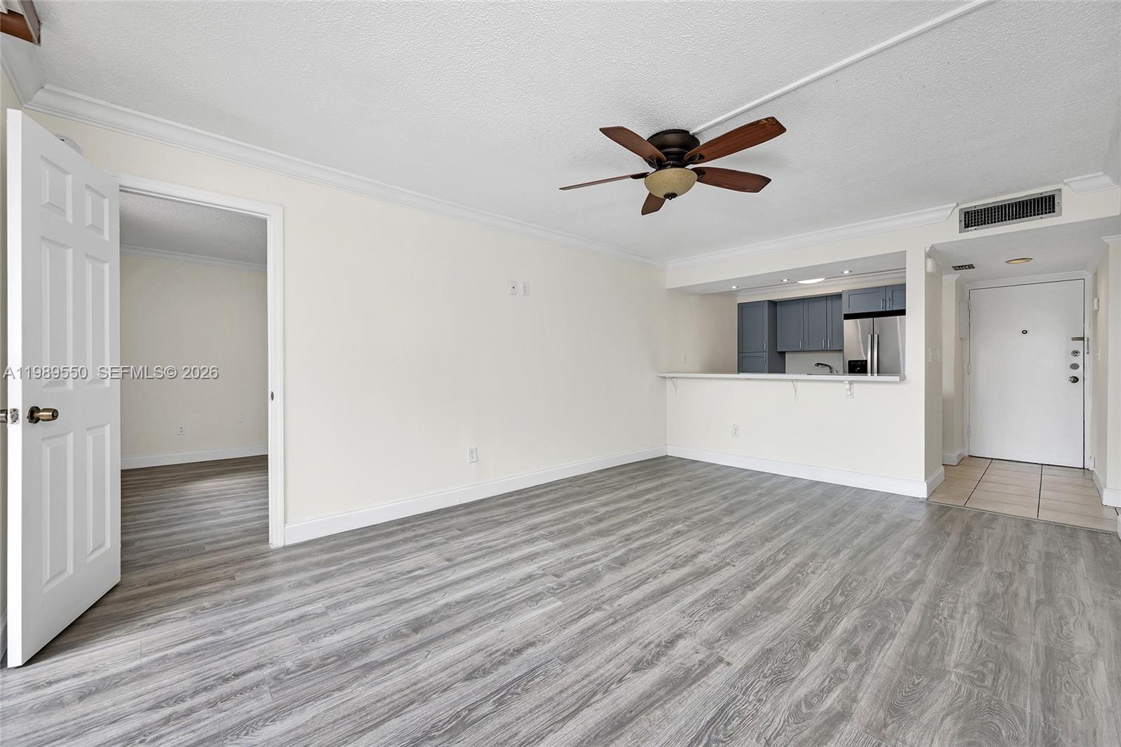 An open-concept living area features gray wood-look flooring, a ceiling fan, and a kitchen pass-through — 14601 N Kendall Dr # 308K, Miami FL 33186, MIAMI, FL