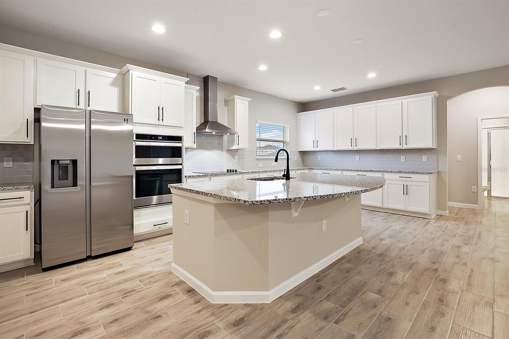 A modern kitchen features white cabinets, stainless steel appliances, granite countertops, and wood-look tile flooring — 3547 CYNTHIA LANE, ORANGE PARK, FL