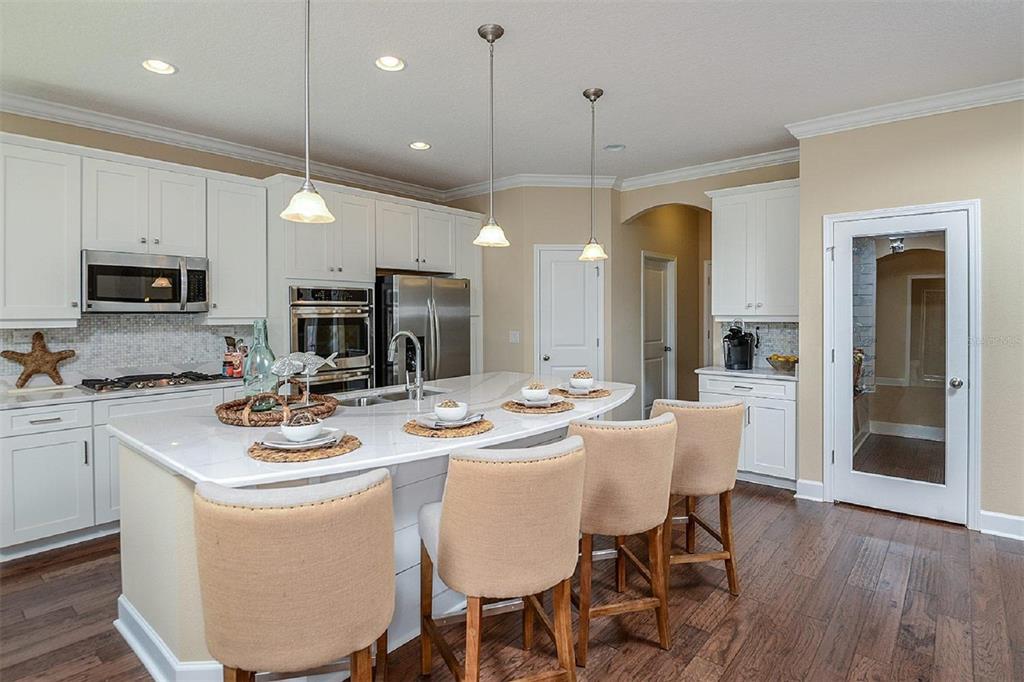 A kitchen features white cabinets, a large quartz island with four chairs, and hardwood floors — 3547 CYNTHIA LANE, ORANGE PARK, FL