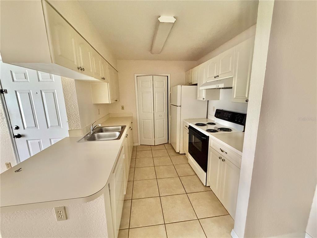 A kitchen features white cabinets, white appliances, a double sink, and tiled flooring — 2550 N ALAFAYA TRAIL UNIT 5105, ORLANDO, FL