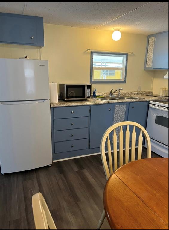 A kitchen features blue cabinets, a white refrigerator, a microwave, and wood-look flooring — 38961 STAPLEY CIRCLE, ZEPHYRHILLS, FL