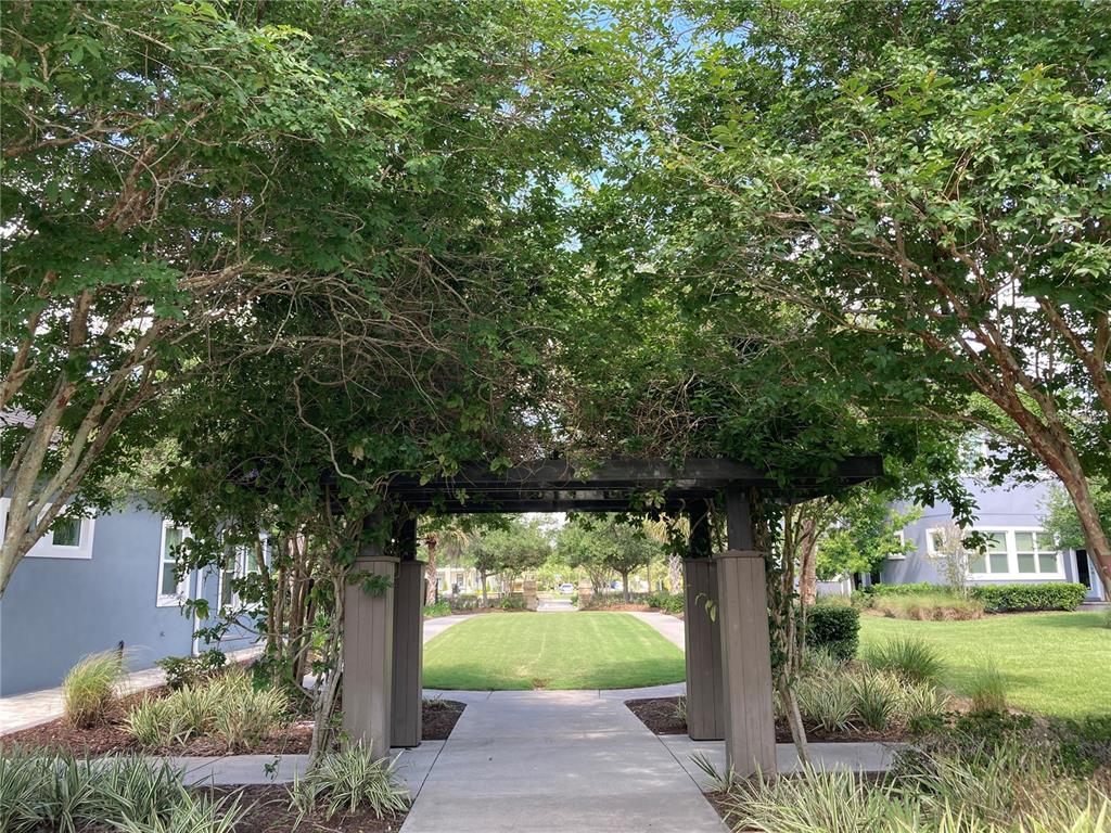 A concrete walkway passes under a wooden pergola surrounded by trees and manicured lawns — 8461 GREIDER WAY, ORLANDO, FL