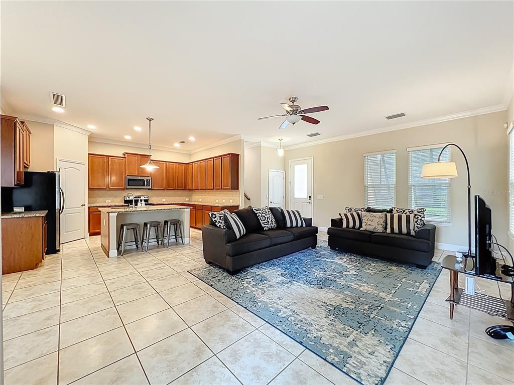 An open-concept living room and kitchen featuring tile floors, dark cabinetry, and two dark sofas — 8461 GREIDER WAY, ORLANDO, FL