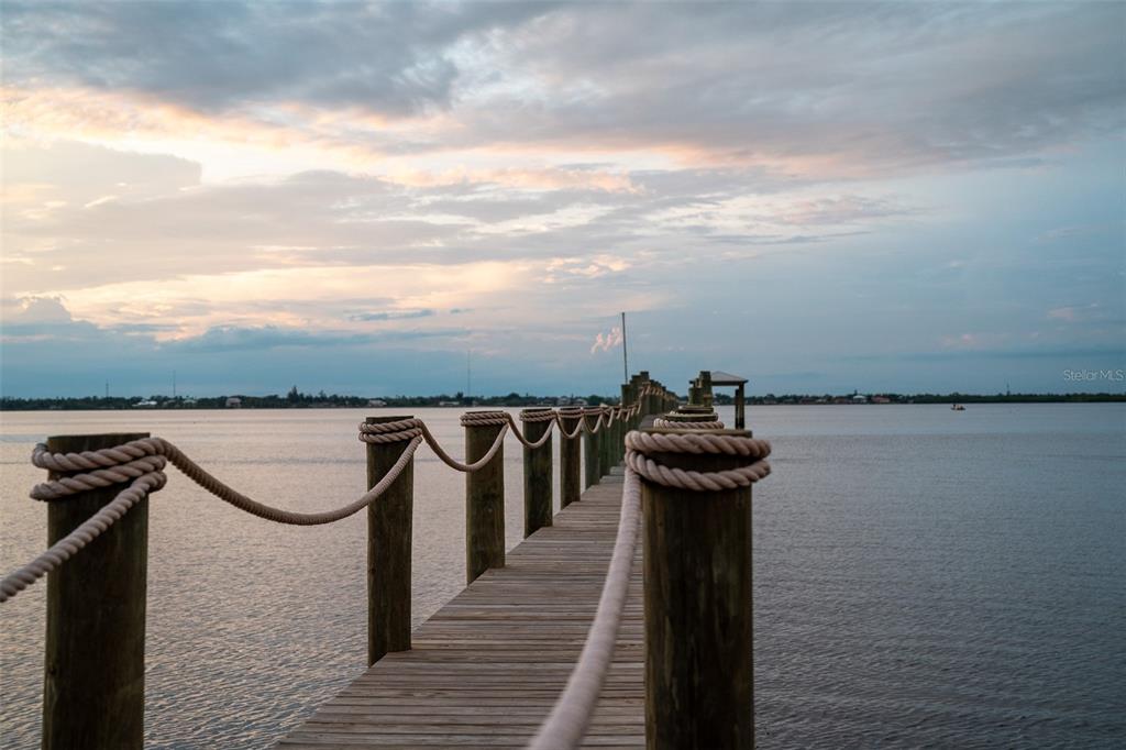 A wooden pier with rope railings extends into a calm body of water at sunset — 25472 SHORE DRIVE, PUNTA GORDA, FL