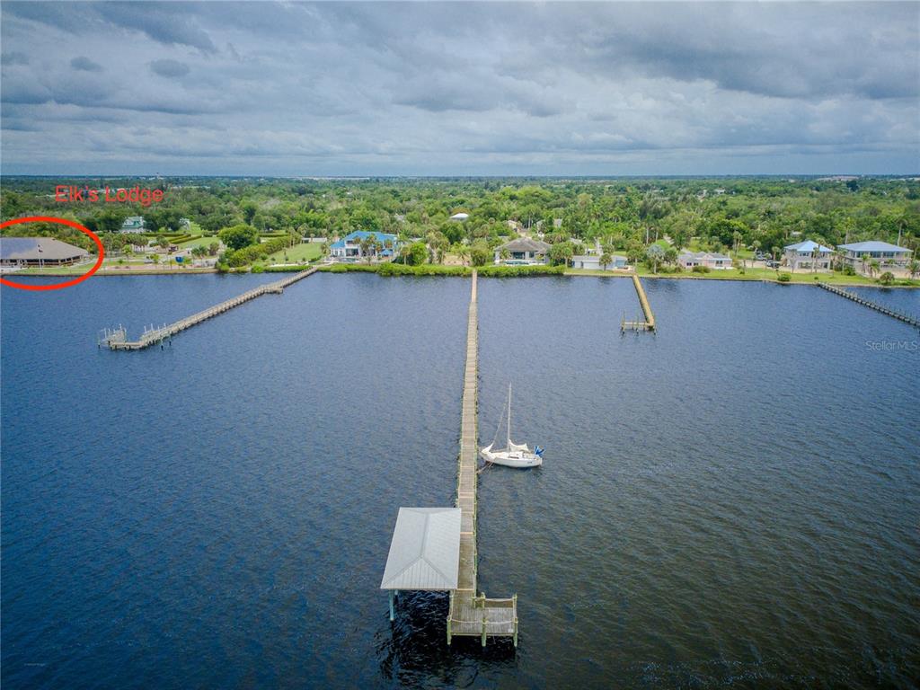 An aerial view shows a long wooden dock extending into a lake near several houses — 25472 SHORE DRIVE, PUNTA GORDA, FL