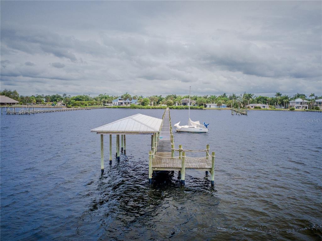 A long wooden dock with a covered boat slip extends into a calm bay — 25472 SHORE DRIVE, PUNTA GORDA, FL