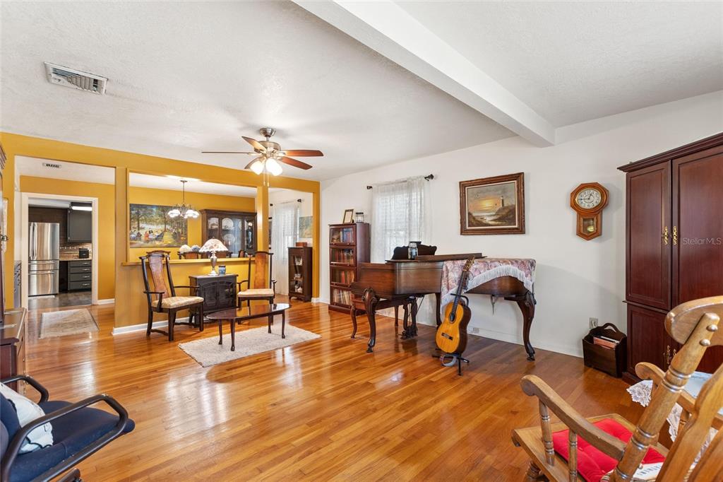 A living room features hardwood floors, a grand piano, and an open view into the kitchen — 2230 W CENTRAL AVENUE, WINTER HAVEN, FL