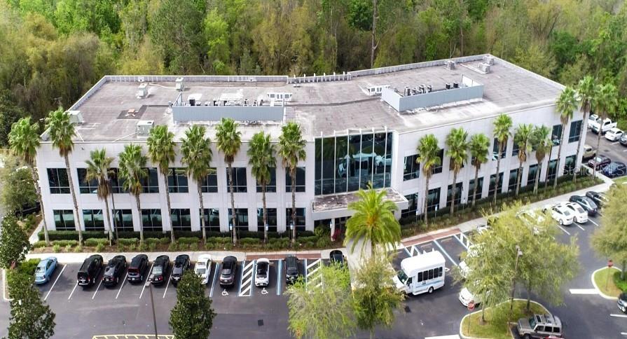 An aerial view shows a multi-story office building with a parking lot and palm trees — 7560 RED BUG LAKE ROAD UNIT 2084, OVIEDO, FL