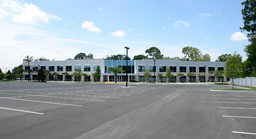 A two-story commercial office building features a large parking lot and surrounding palm trees — 7560 RED BUG LAKE ROAD UNIT 2084, OVIEDO, FL