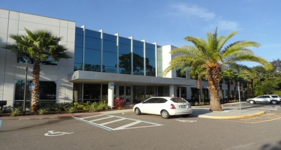A white car is parked in front of a modern office building with palm trees — 7560 RED BUG LAKE ROAD UNIT 2084, OVIEDO, FL