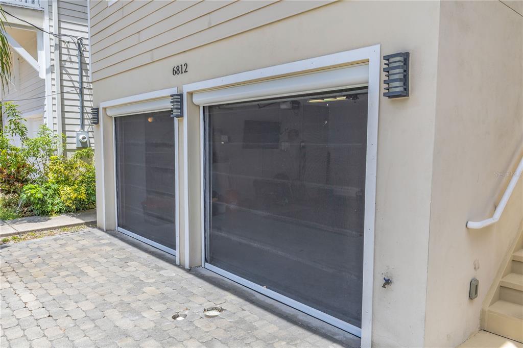 A two-car garage exterior features retractable mesh screens over the openings and a paved driveway — 6812 S KISSIMMEE STREET, TAMPA, FL