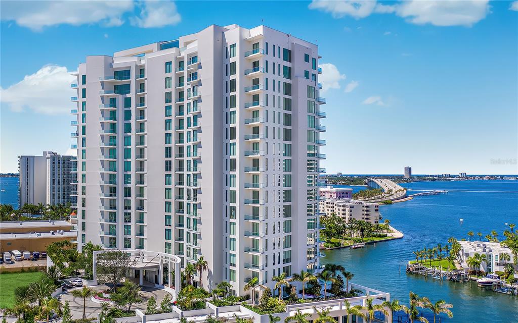 An aerial view of a tall white residential building next to a bay and bridge — 401 QUAY COMMONS UNIT 1501, SARASOTA, FL