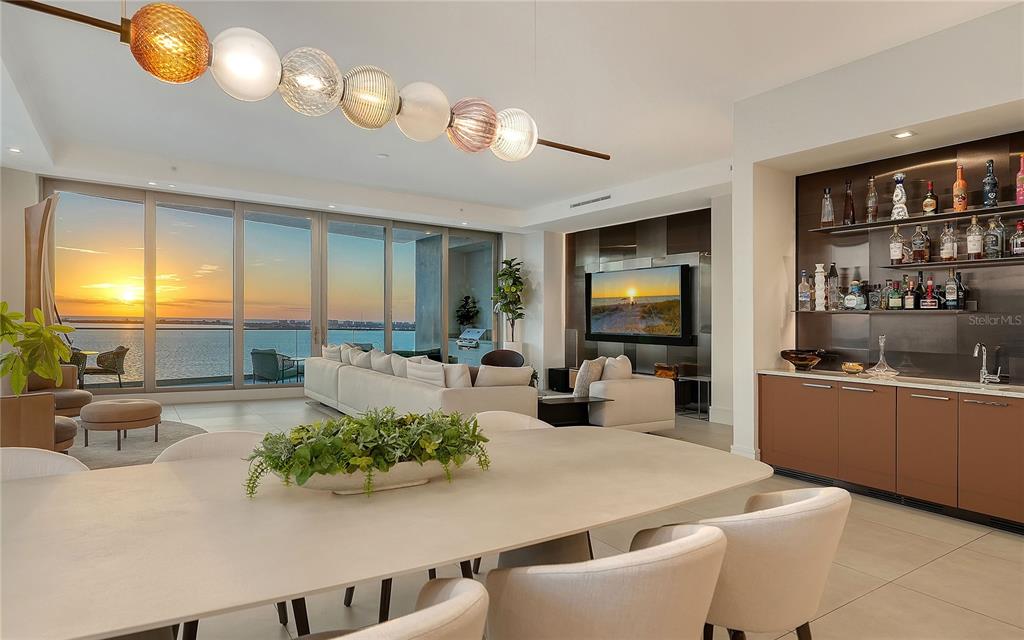 A modern living and dining area features a wet bar, floor-to-ceiling windows, and ocean views — 401 QUAY COMMONS UNIT 1501, SARASOTA, FL