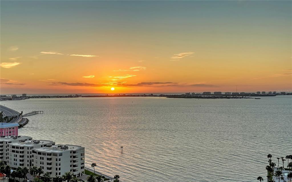 An elevated view of a sunset over a bay with coastal buildings and a bridge — 401 QUAY COMMONS UNIT 1501, SARASOTA, FL