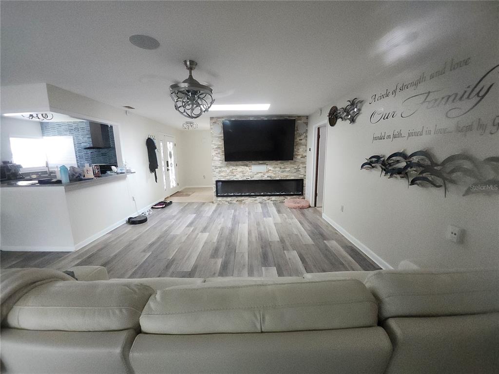 A living room features a stone fireplace wall with a mounted television and wood-look flooring — 4 CHIPPEWAY COURT, PALM COAST, FL