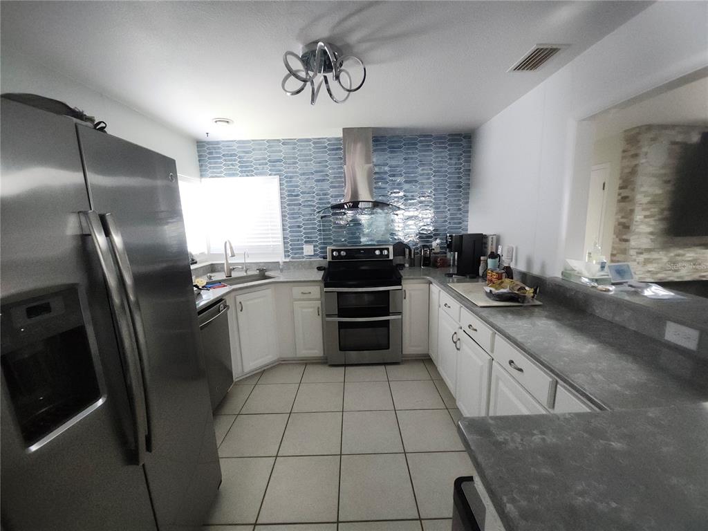 A kitchen features stainless steel appliances, white cabinets, gray countertops, and a blue tiled backsplash — 4 CHIPPEWAY COURT, PALM COAST, FL