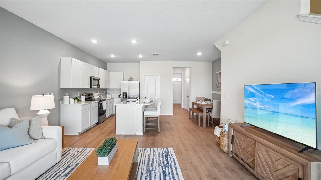 An open-concept living room and kitchen featuring white cabinetry, wood flooring, and a television — 12607 CITRUS PARK LANE, TAMPA, FL