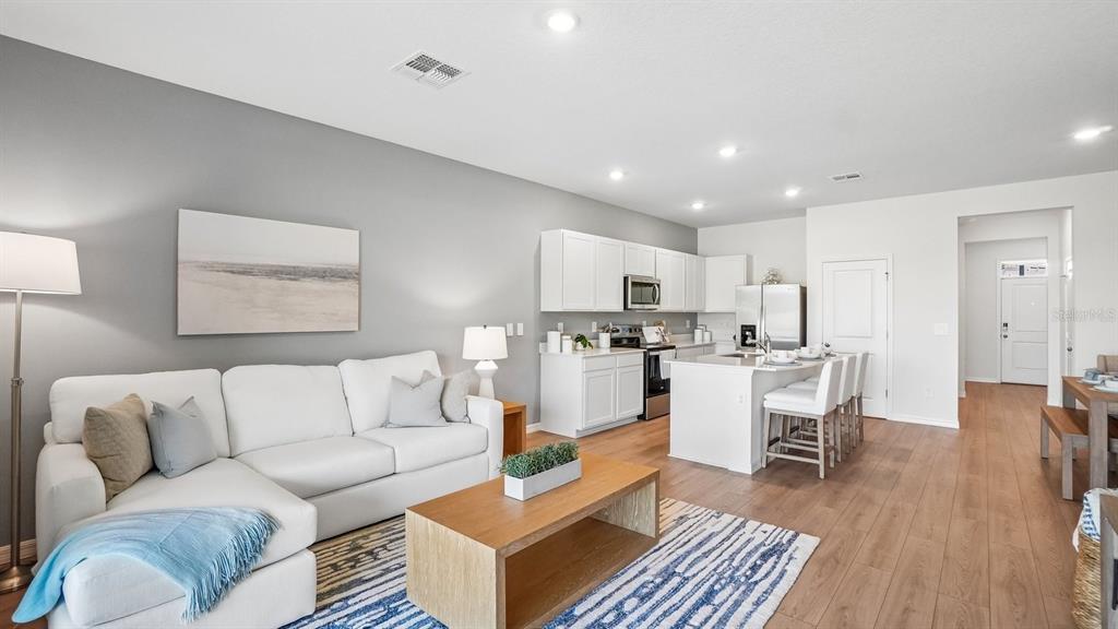 A bright open-concept living room and kitchen featuring white cabinetry, wood flooring, and neutral furniture — 12607 CITRUS PARK LANE, TAMPA, FL