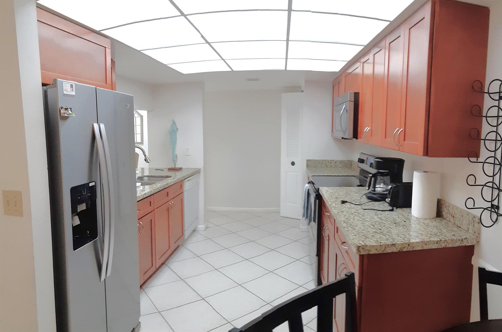 A galley kitchen features orange wood cabinets, granite countertops, stainless steel appliances, and tile flooring — 750 Egret Circle # 6404, Delray Beach FL 33444, DELRAY BEACH, FL