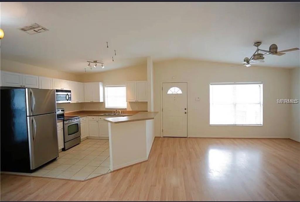 A kitchen with white cabinets and stainless steel appliances opens to a light-floored living area — 1717 W NASSAU STREET UNIT A, TAMPA, FL