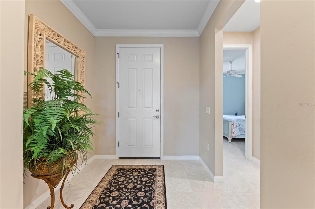 A foyer features a white front door, a decorative mirror, a potted fern, and tile flooring — 13825 RINUCCIO STREET, VENICE, FL