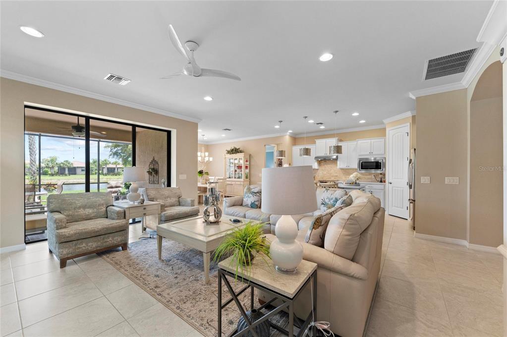 An open-concept living room features tile flooring, neutral walls, a ceiling fan, and kitchen access — 13825 RINUCCIO STREET, VENICE, FL