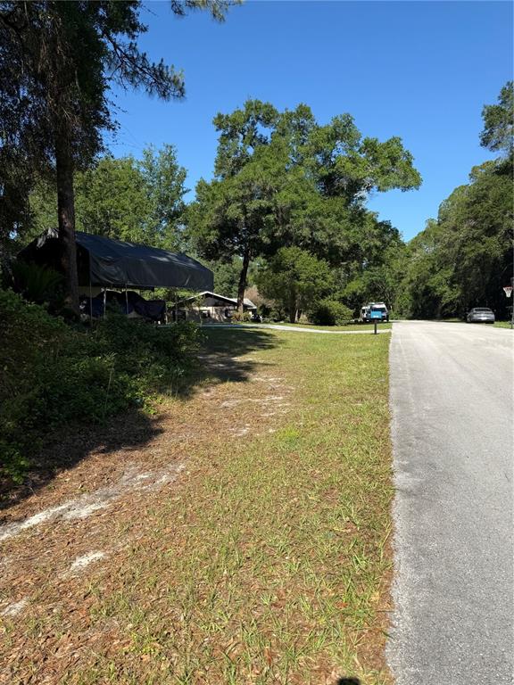A gravel road runs alongside a grassy yard with a covered carport and mature trees — 10927 N AIRWAY LOOP, CITRUS SPRINGS, FL