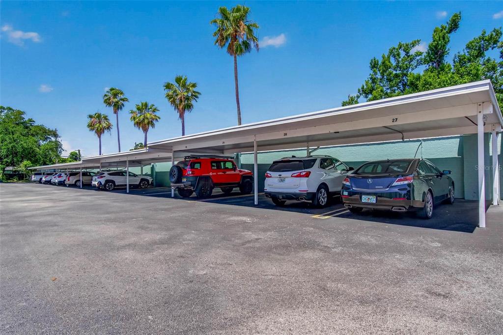 A row of covered parking spaces with several parked vehicles under a blue sky — 701 POINSETTIA ROAD UNIT 308, BELLEAIR, FL