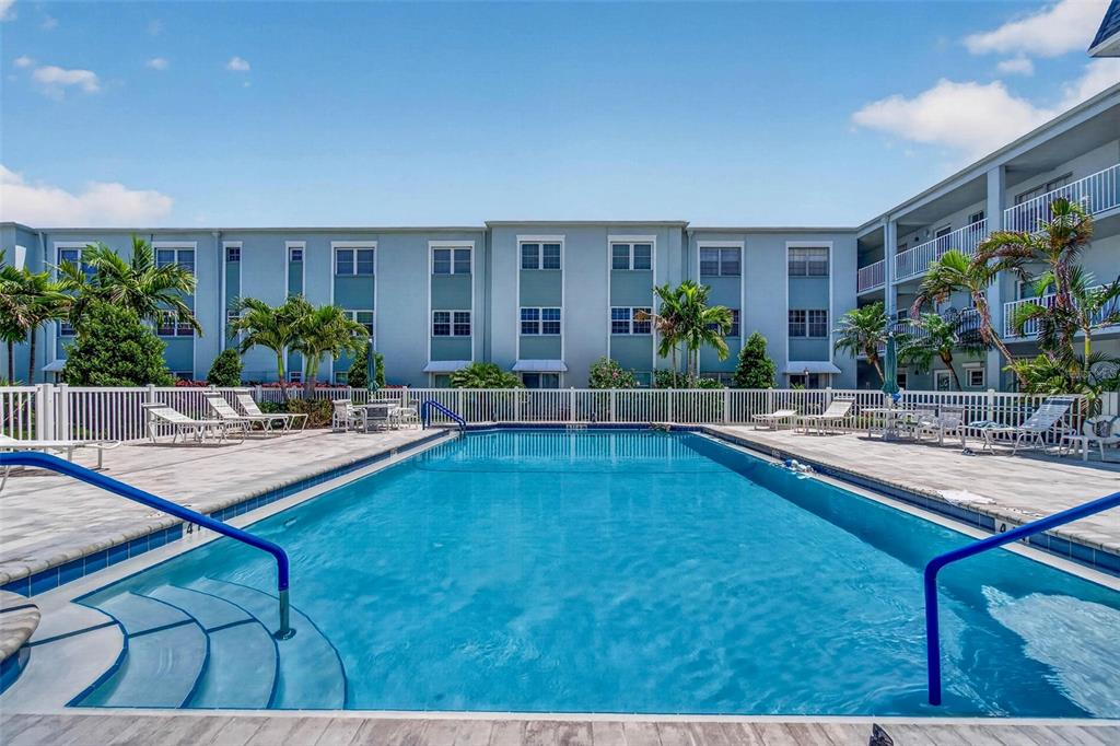 A rectangular swimming pool is surrounded by a white fence and a multi-story apartment building — 701 POINSETTIA ROAD UNIT 308, BELLEAIR, FL