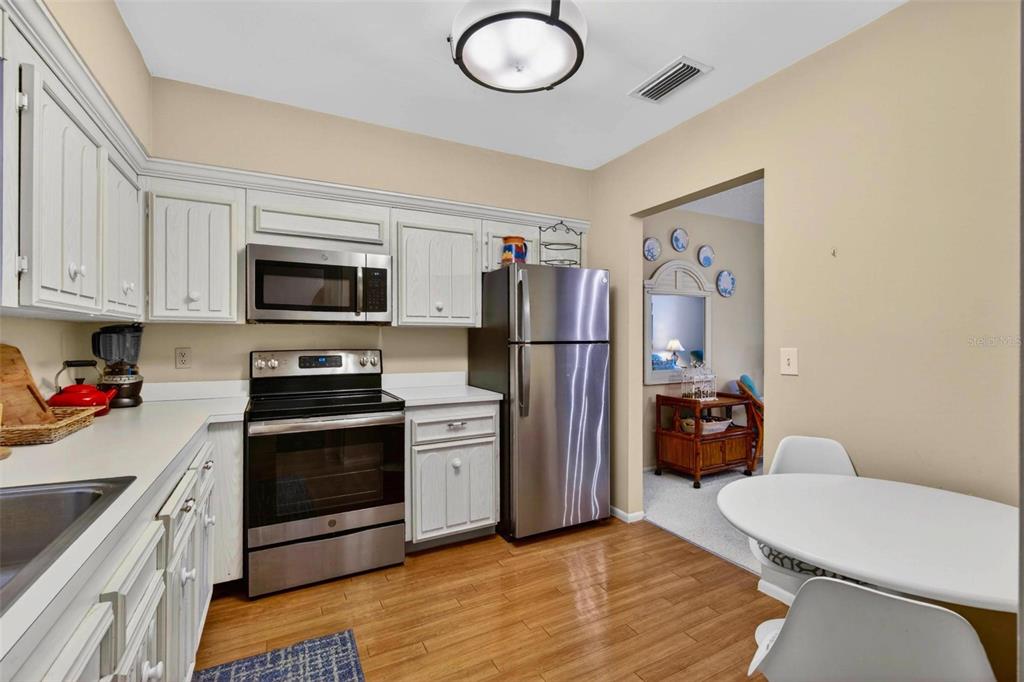 A kitchen features white cabinets, stainless steel appliances, and wood flooring next to a dining area — 701 POINSETTIA ROAD UNIT 308, BELLEAIR, FL