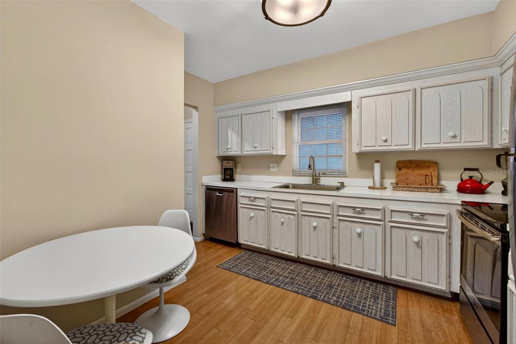 A kitchen features light wood cabinets, white countertops, a small dining table, and wood flooring — 701 POINSETTIA ROAD UNIT 308, BELLEAIR, FL