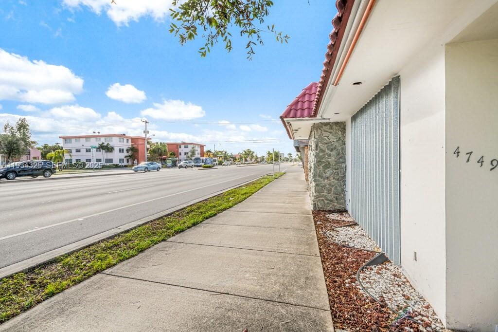 A sidewalk runs alongside a building exterior with a stone pillar and metal shutters — 4749 Hollywood Blvd, Hollywood FL 33021, HOLLYWOOD, FL