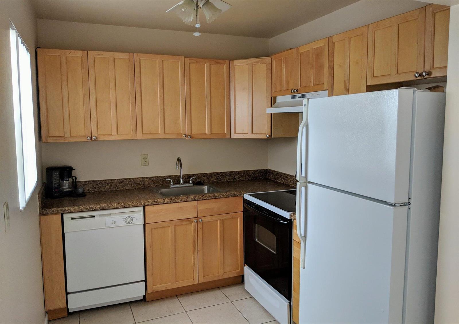 A kitchen features light wood cabinets, granite-look countertops, white appliances, and tiled flooring — 288 Norwich, West Palm Beach FL 33417, WEST PALM BEACH, FL