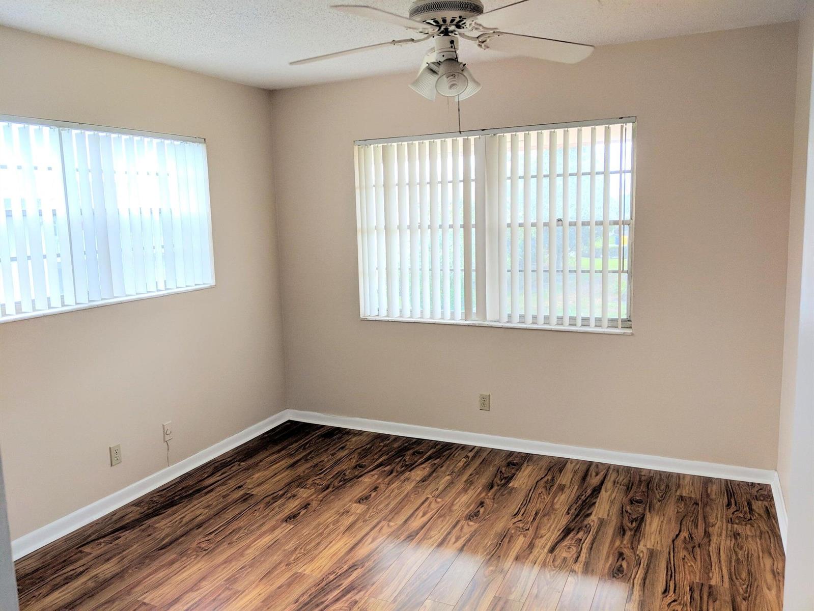 An empty bedroom features beige walls, wood-look laminate flooring, vertical blinds, and a ceiling fan — 288 Norwich, West Palm Beach FL 33417, WEST PALM BEACH, FL